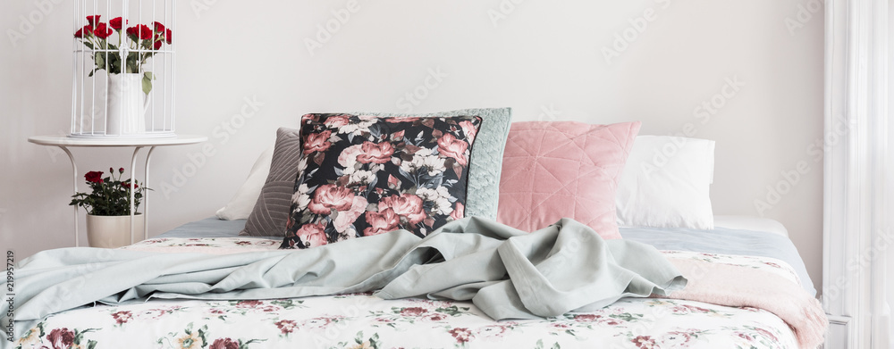Panorama of floral pillow and blue blanket on bed in bright feminine bedroom interior. Real photo - obrazy, fototapety, plakaty 