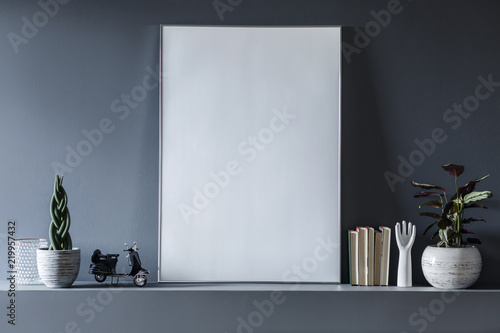 Real photo of a mockup poster standing on shelf between the plants and ornaments in grey room interior photo