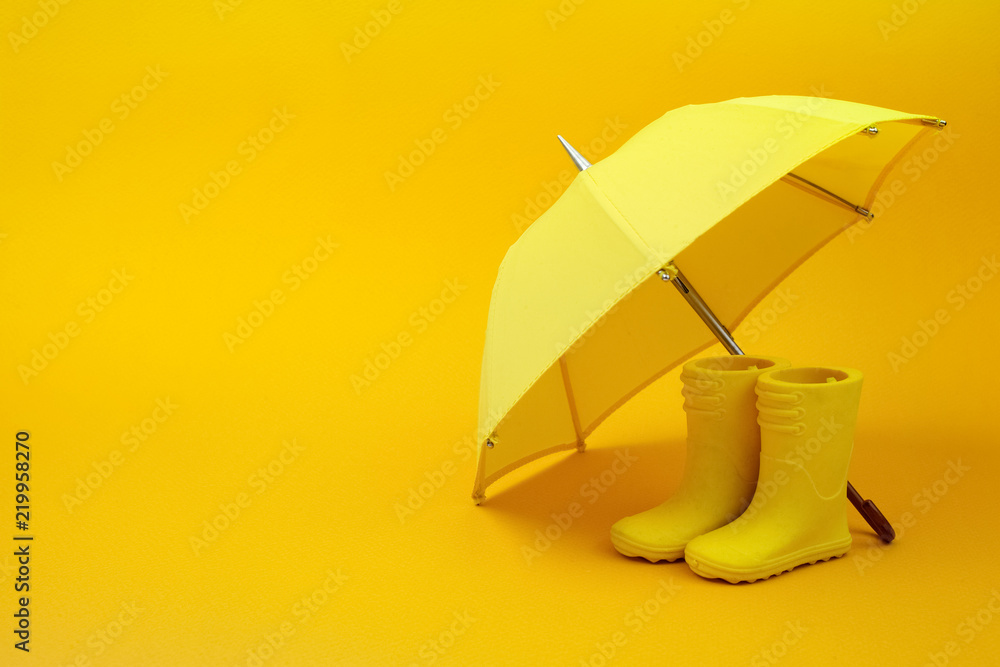 A pair of yellow rain boots and a umbrella on a yellow - obrazy, fototapety, plakaty 