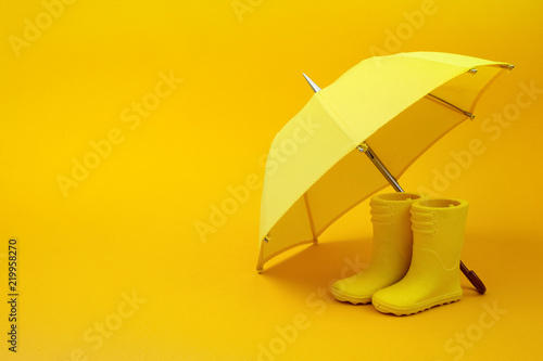 A pair of yellow rain boots and a umbrella on a yellow