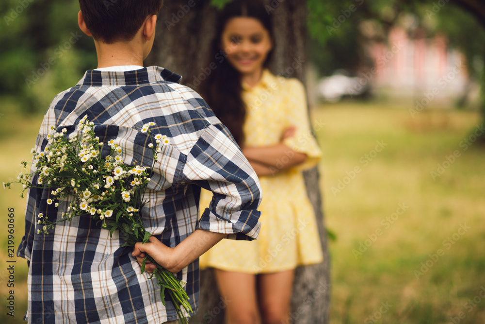 Young boy giving flowers to girl. Sweet little boy holding bouqet of flowers behind his back to