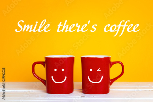 Two red coffee mugs with a smiling faces on a yellow background with the phrase Smile there's coffee.