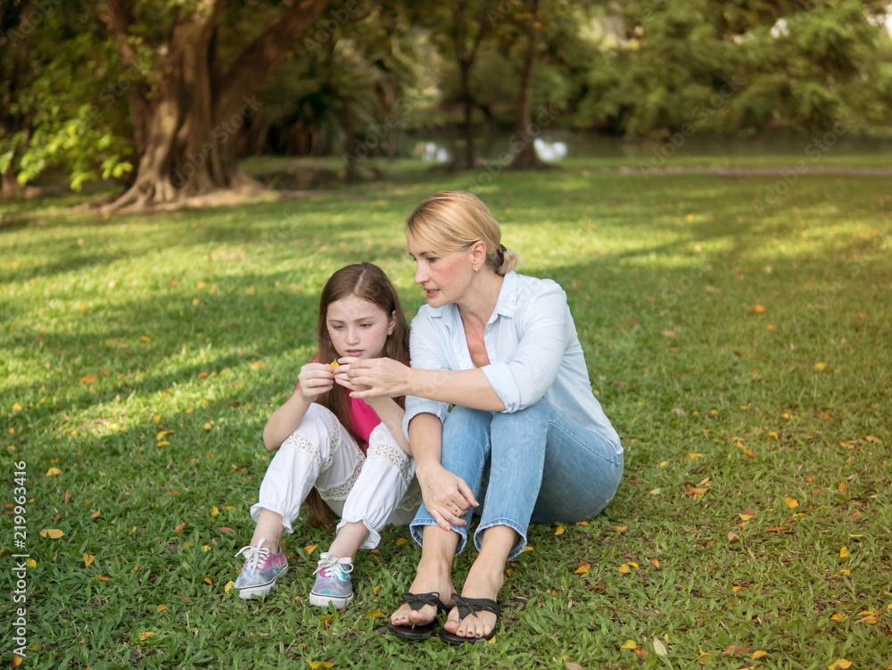 Mother and daughter sitting and playing together in the park. Happy family resting together on green grass. Happy family concept. Mother and daughter sitting and playing together in the park. Happy family resting together on green grass. Happy family concept.