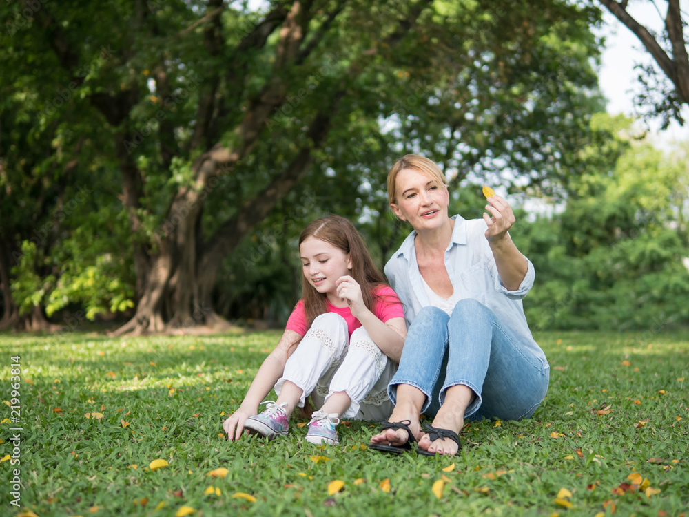Fototapeta premium Mother and daughter sitting and playing together in the park. Happy family resting together on green grass. Happy family concept.