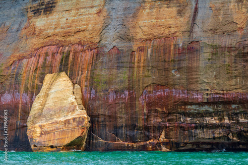A mitten shaped rocks against the a stone cliff at Pictured Rocks National Lakeshore in Northern Michigan. These mineral laden cliffs have a painted look in the sandstone rock formations