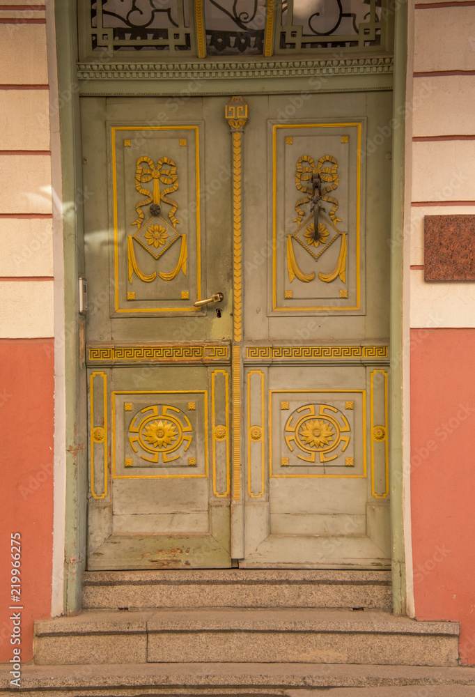 Fancy old green wooden doors with yellow design. There are three stone steps leading up to doorway.