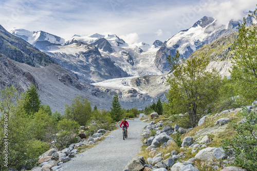 Senior woman, riding her e-mountain bike on the trail to the Morteratsch glacier near Pontresina , Engadin, Switzerland,Alps. In the background the famous mountains of Piz palu, Bellavista, Bernina photo