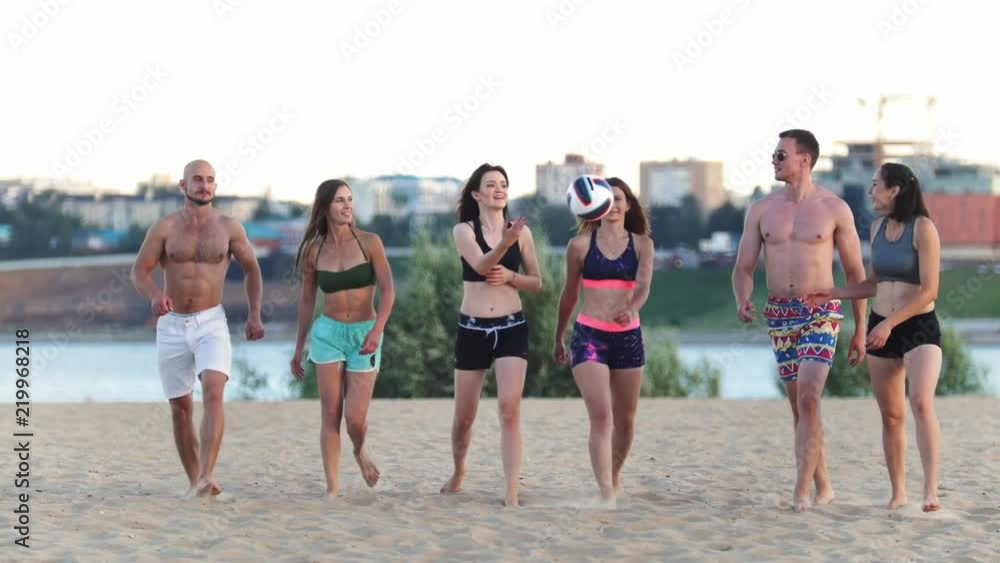 Beautiful young sports men and women walking on the beach after a game of volleyball, talking, smiling, laughing Beautiful young sports men and women walking on the beach after a game of volleyball, talking, smiling, laughing