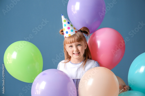 Cute little girl in Birthday hat and with balloons on color background