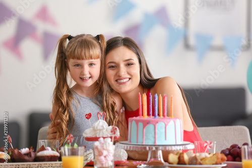 Cute little girl and her mother with birthday cake at table