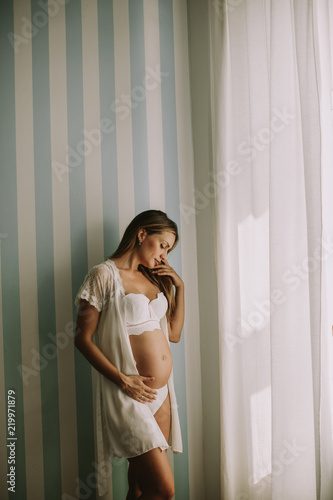 Young pregnant woman standing by the window