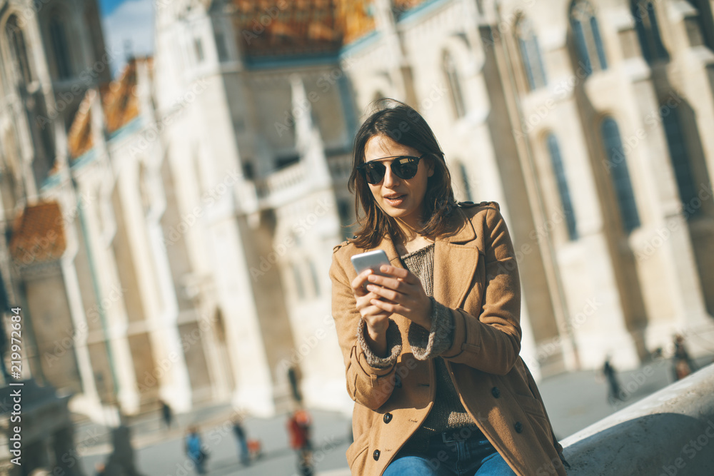 Obraz premium Trendy young woman sitting outdoor and using mobile phone