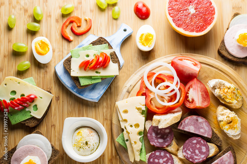 Breakfast table with cheese sandwiches, sausage, vegetables, hard boiled eggs and fruits