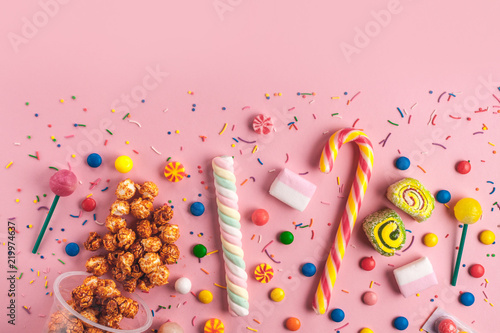 Colored, children's, unhealthy candy, marmalade, marshmallow, caramel popcorn, chupa-chups on a pink background. A table full of sweets. Top view