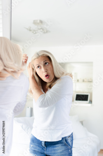 Senior woman checking hair in front of mirror