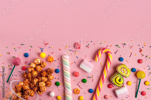 Colored, sugar, sweet candy, marmalade, marshmallow, caramel popcorn, chupa-chups on a pink background. A table full of sweets. Copy space. Top view
