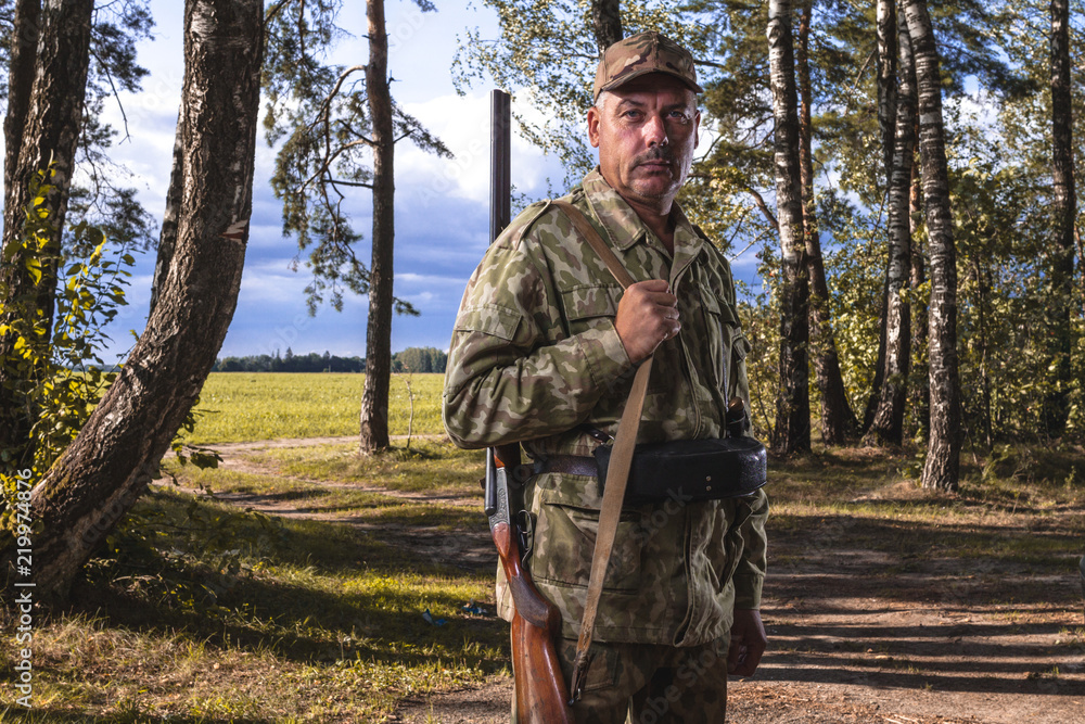 Portrait of a hunter with a hunting gun in the autumn forest. Copy space