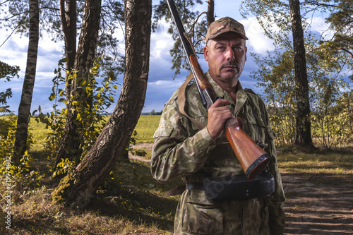 Portrait of a hunter with a hunting gun and in the form of a background of trees in the forest.