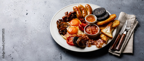 Full fry up English breakfast with fried eggs, sausages, bacon, black pudding, beans and toasts on gray concrete background photo