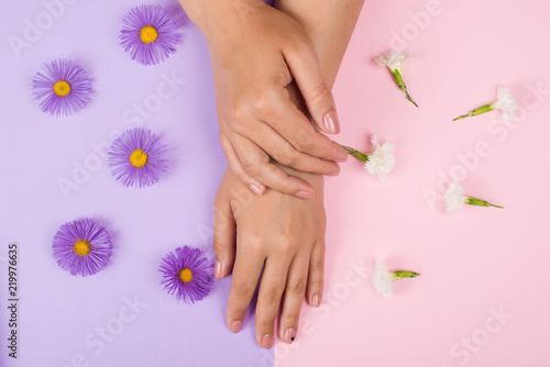 Female manicure background. Hand and nail care. Beautiful young woman s hands on pink and purple background with flowers. Hand with pastel nails. Stylish trendy women manicure.