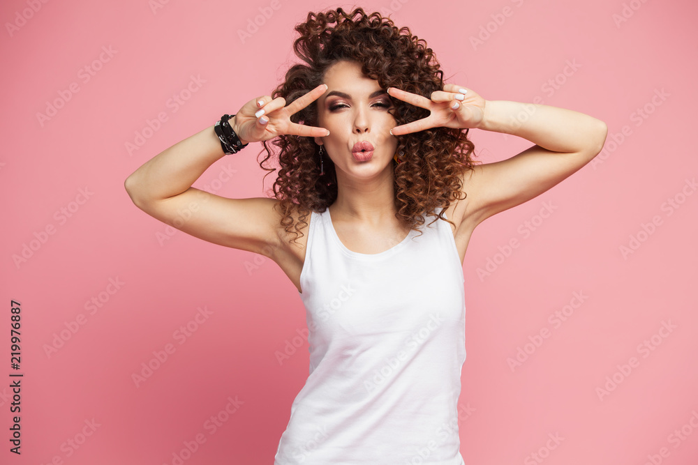 Image of happy young woman standing isolated over pink background showing peace gesture. Looking camera Image of happy young woman standing isolated over pink background showing peace gesture. Looking camera