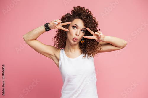 Image of happy young woman standing isolated over pink background showing peace gesture. Looking camera