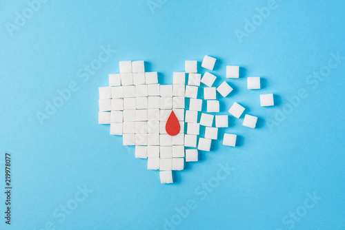 a drop of blood on broken heart made of pure white cubes of sugar isolated on blue background, World diabetes day