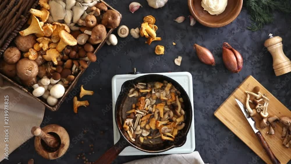 Top view of preparation and frying of edible wild mushrooms. Mix of chanterelle, portobello, shiitake in Cast-iron pan. Cooking with spices, butter, parsley, onion, leek, garlic. Top view of preparation and frying of edible wild mushrooms. Mix of chanterelle, portobello, shiitake in Cast-iron pan. Cooking with spices, butter, parsley, onion, leek, garlic.