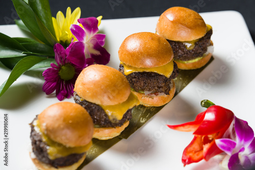 Row of four cheese burger sliders on white plate