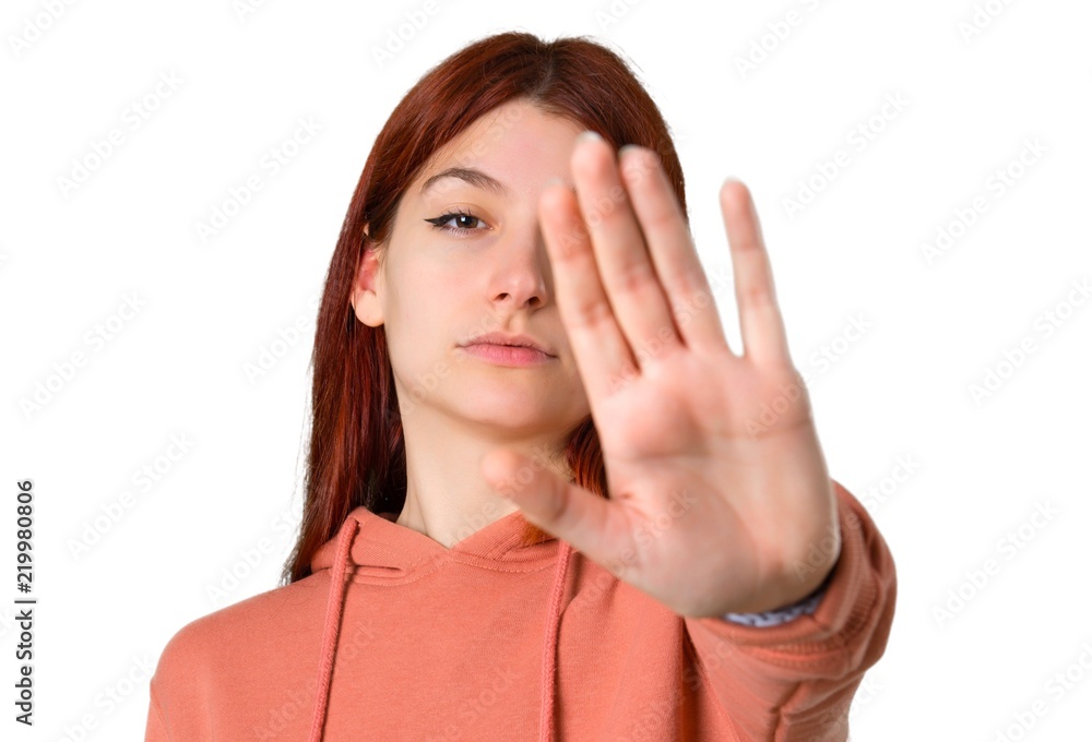 Young redhead girl with pink sweatshirt making stop gesture with her hand denying a situation that thinks wrong on isolated white background Young redhead girl with pink sweatshirt making stop gesture with her hand denying a situation that thinks wrong on isolated white background