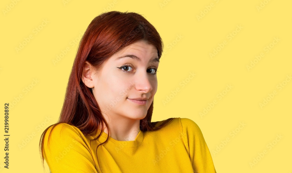 Young redhead girl with yellow sweater making unimportant and doubts gesture while lifting the shoulders on isolated yellow background Young redhead girl with yellow sweater making unimportant and doubts gesture while lifting the shoulders on isolated yellow background