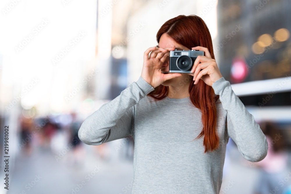 Young redhead girl holding a camera on unfocused background