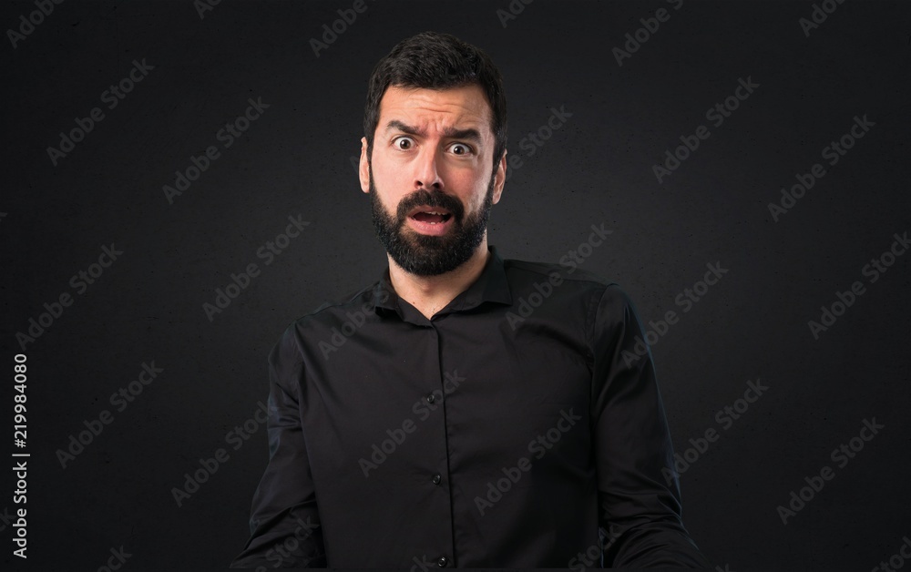 Handsome man with beard stressed overwhelmed on black background