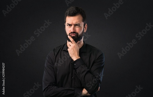 Handsome man with beard thinking on black background