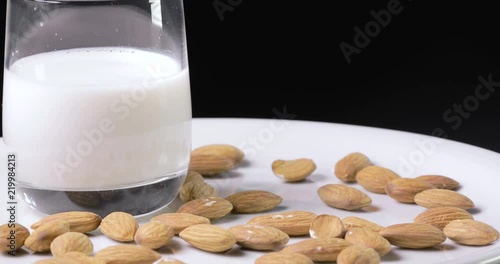 Latte di mandorla in un bicchiere disposto su un piatto bianco rotante con mandorle 