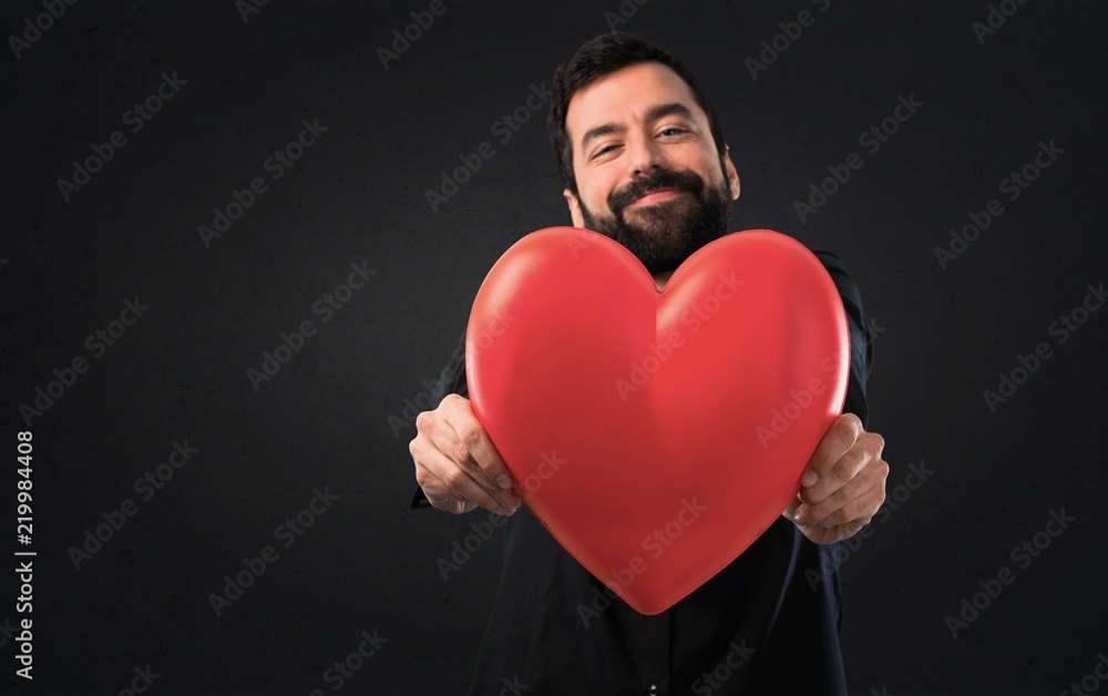 Handsome man with beard holding a heart toy on black background Handsome man with beard holding a heart toy on black background