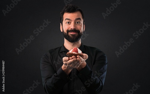 Handsome man with beard with pastry on black background