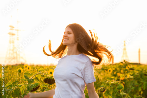 Summer portrait of happy young woman in white with flying hair in sunflower field 