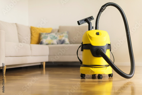 Yellow modern vacuum cleaner in living room. Copy space. Flat clean vacuuming concept photo