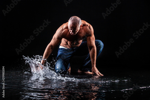 very muscular handsome athletic man striking with a hand on water