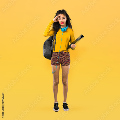 Full body of Teenager student girl with curly hair with surprise and shocked facial expression. Gaping because can not believe what is happening on yellow background