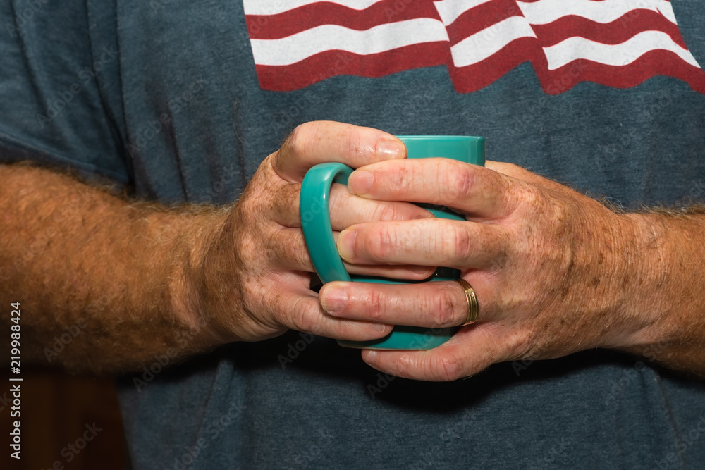 Fototapeta premium Senior male hands with age spots holding morning coffee in two hands