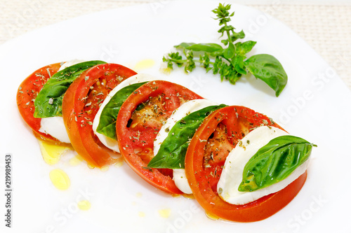 Caprese salad, slices of mozzarella and tomato, with basil and oregano.