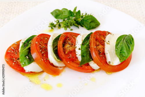 Caprese salad, slices of mozzarella and tomato, with basil and oregano.
