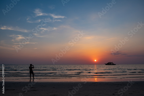 Silhouette of a man taking photos with mobile phone on the beach during sunset