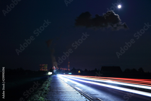 Światła samochodów w nocy i elektrownia w świetle księżyca w pełni.