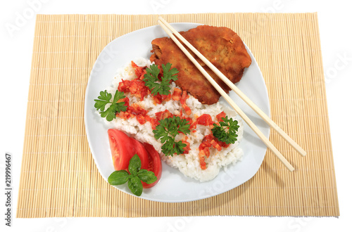 Ryż na białym talerzu z kotletem schabowym, sosem, pomidorem, zieloną petruszką i bazylią.