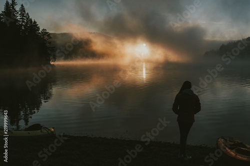 Woman watching the sunrise on foggy lake