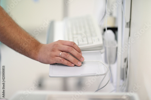 The doctor's hand on a computer mouse near the computer keyboard in the operating room