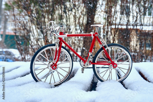 A toy model of a red bicycle made of metal, executed with good accuracy, is in winter in snowdrifts and cold weather on a city street